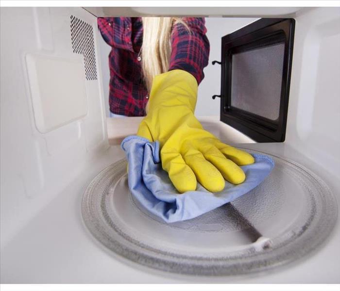 hand with plastic glove cleaning the inside of a microwave
